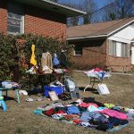 Clothes and household items laid out for a yard sale in front of a house