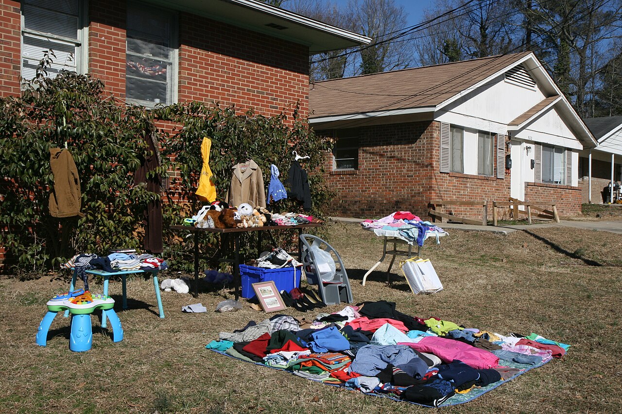 Clothes and household items laid out for a yard sale in front of a house